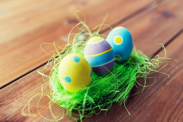 easter, holidays, tradition and object concept - close up of colored easter eggs and decorative grass on wooden surface
