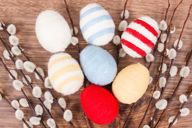 Easter catkins and eggs wrapped woolen string on rustic board, festive decoration concept